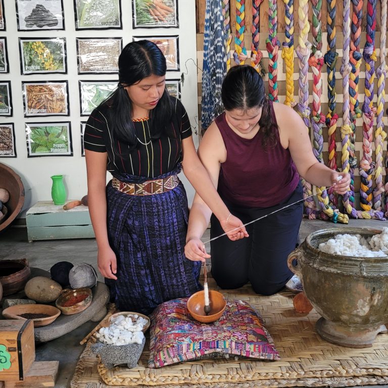 Two people kneeling on the ground, surrounded by a variety of baskets and pots.