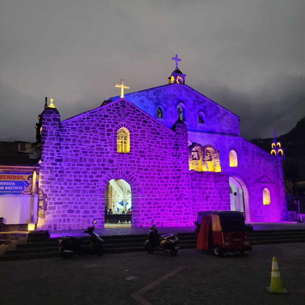 The facade of a stone church, lit up with purple and blue lights.