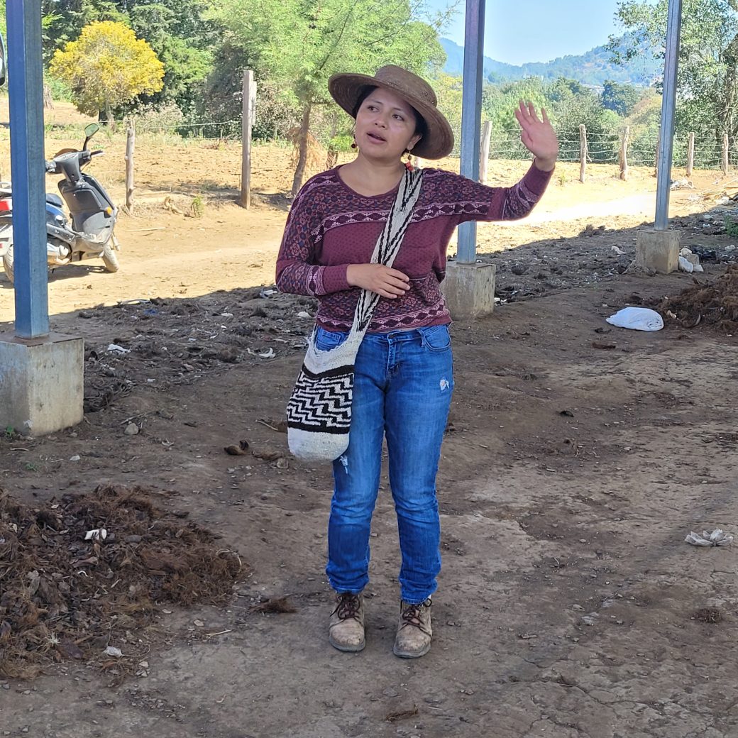 A women speaking, standing on a compacted dirt floor.