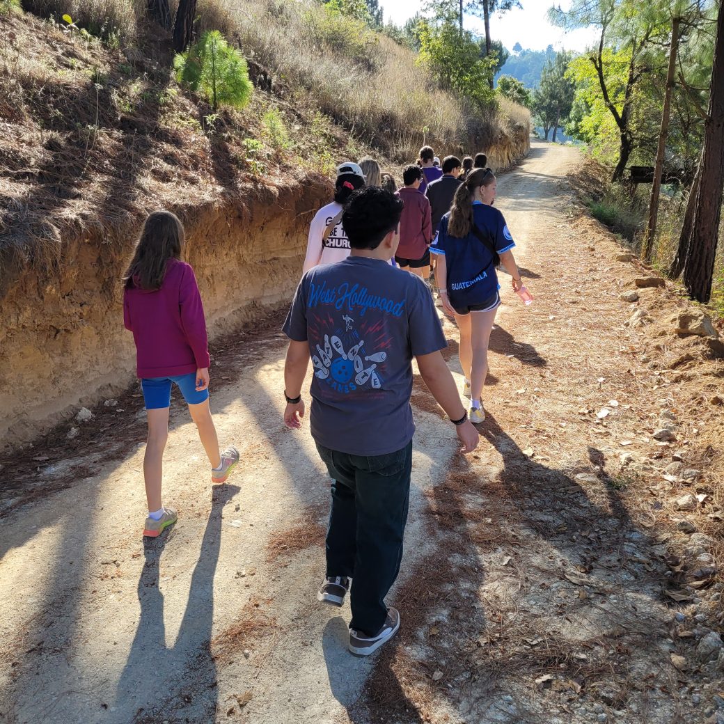 A group of people walking on a dirt path in the morning sun.