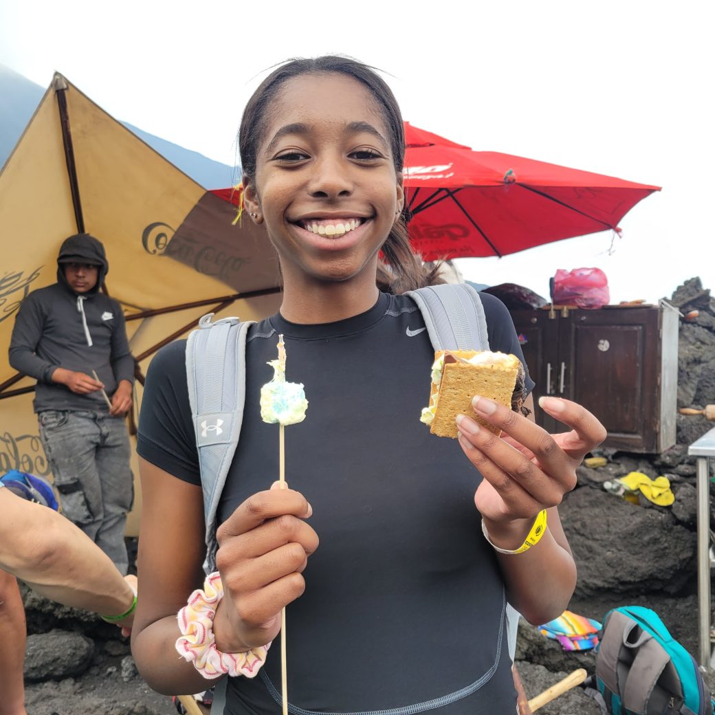 A woman poses with a roasted marshmallow and a s'more.