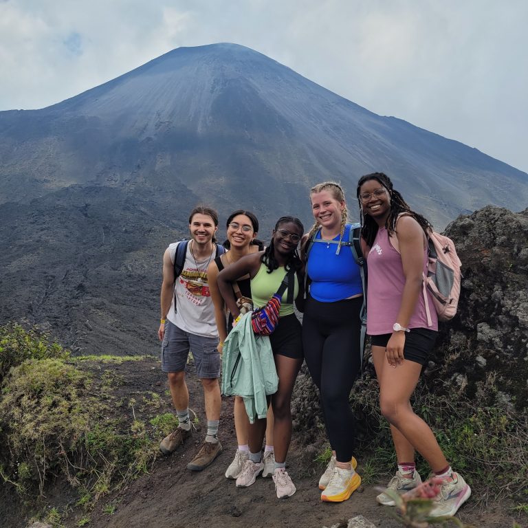 A group of five people pose on a mountaintop.