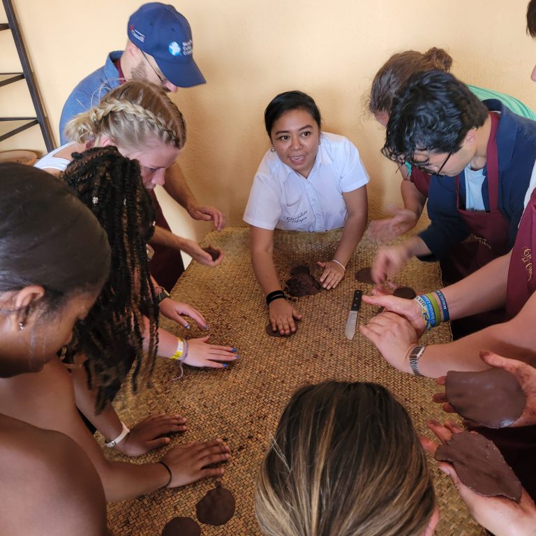 A group of people gathered around a table, rolling and shaping a dark paste with their hands.