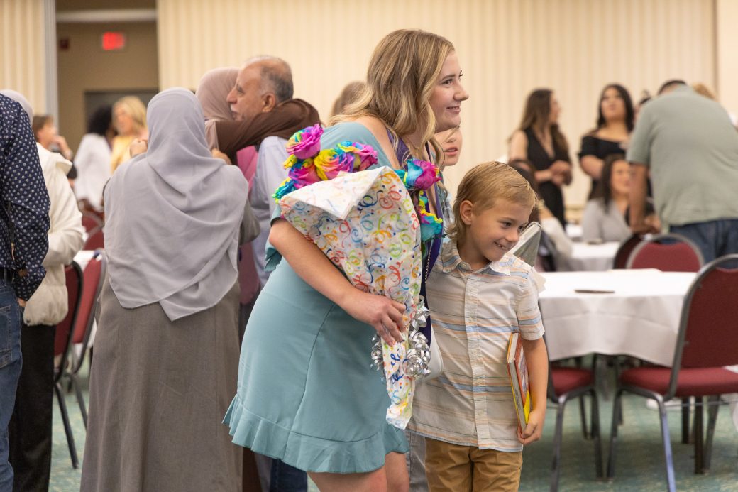 Nursing graduate hugging younger sibling and holding flowers