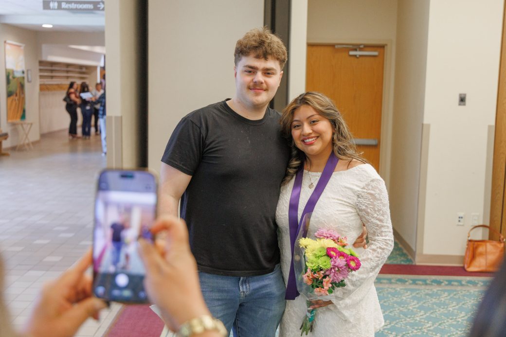 Nursing graduate standing next to friend and holding flowers