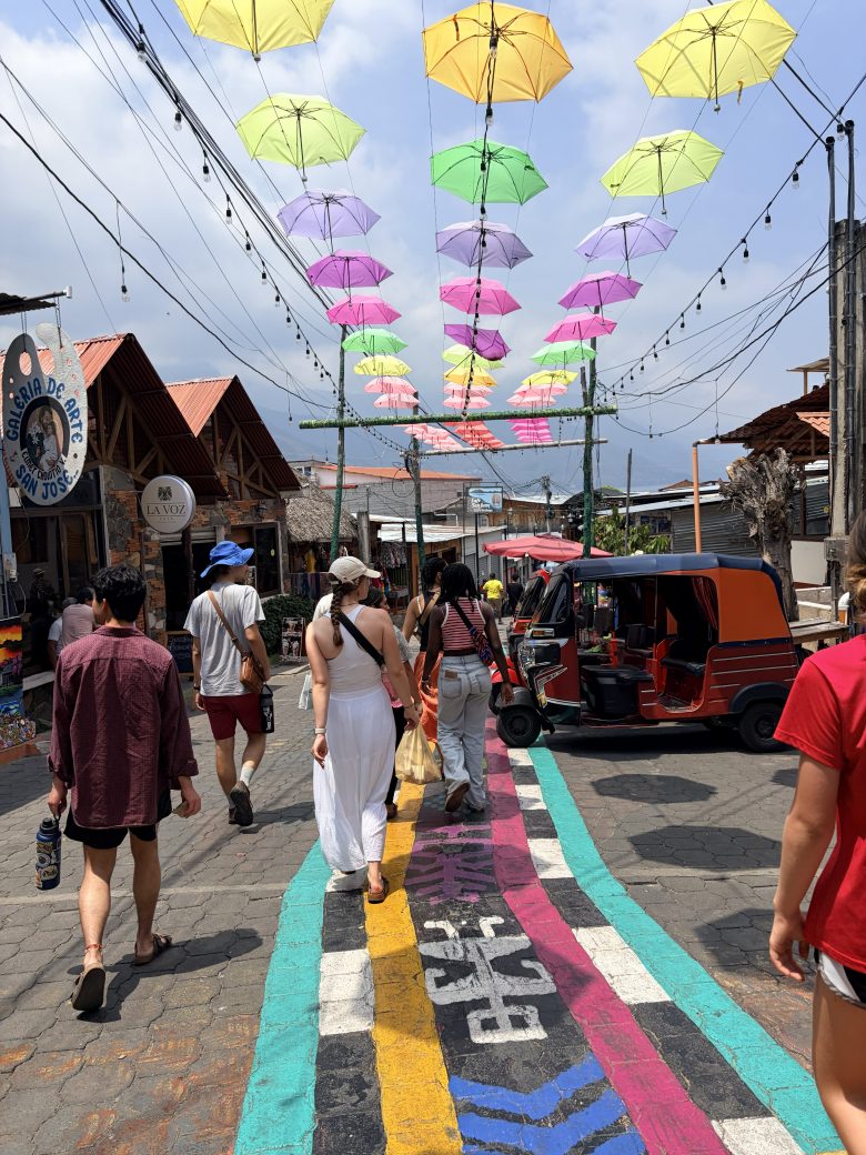 People walking down a brightly colored street, with umbrellas hanging overhead.