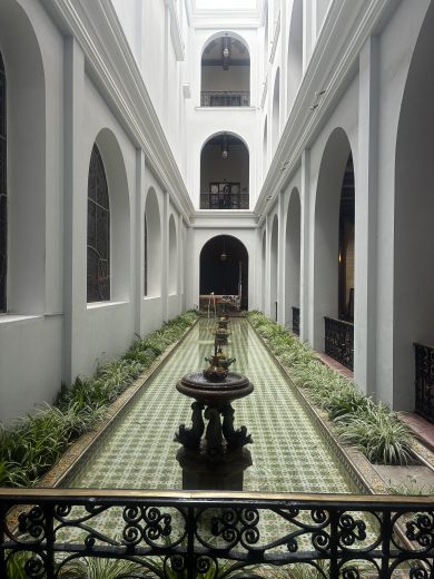 A fountain in a long shallow pool surrounded by white pillars.