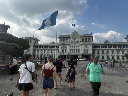 People walking across a plaza towards a large green palace.