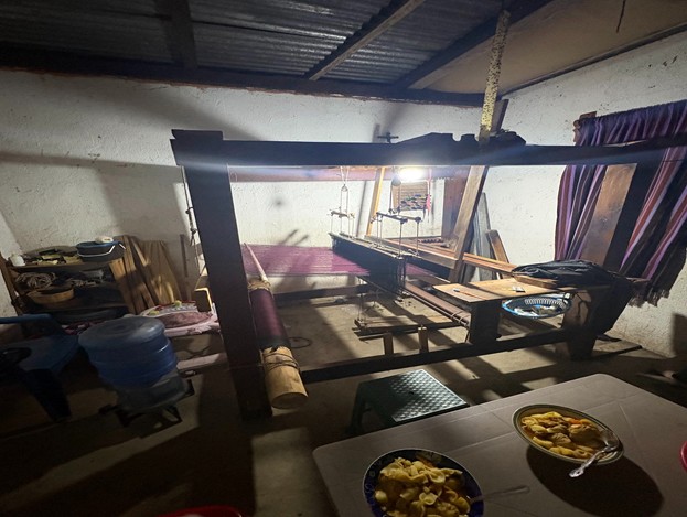 A lowlit room filled with a loom and a table with two dishes of food.
