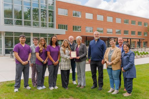 Ten people stand in front of Westlawn Hall with an award