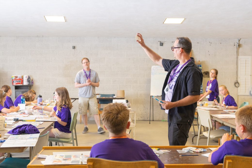 Teacher raises hand to show students how to create art trading card