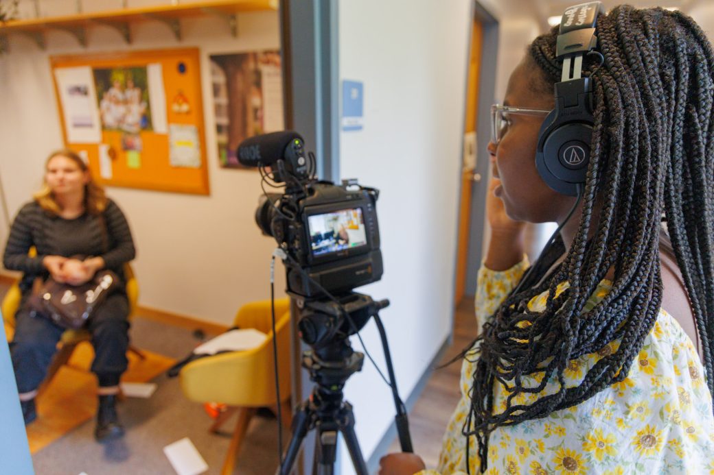 One student films with camera while another student acts behind camera for summer film camp