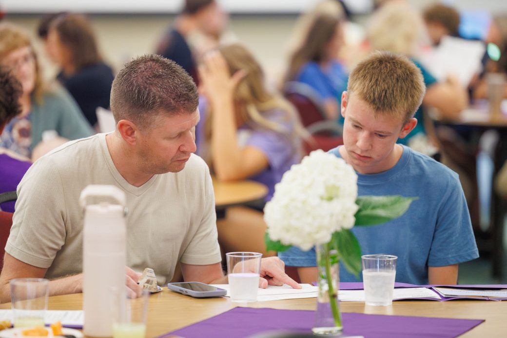 Dad and incoming student son talk about schedule at their table