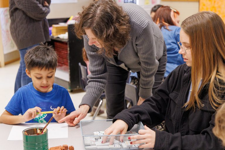 Kathy Meyer Reimer helping a student and child theough a classroom activity.