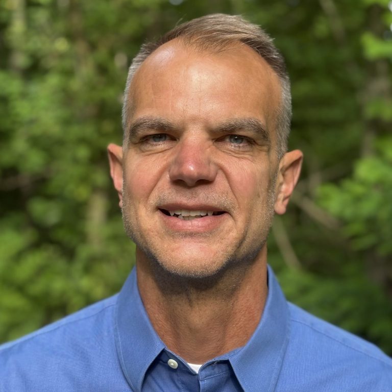 headshot of Jason Kissel wearing a blue button up in an outdoor setting