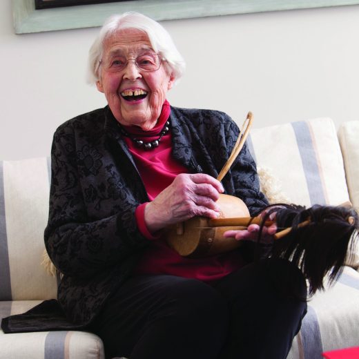Mayer Oyer in her living room playing a traditional African instrument and laughing at someone behind the camera