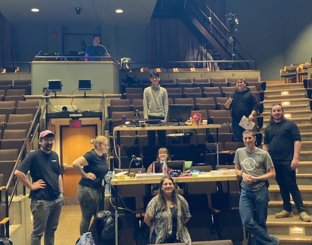 a group of 9 student and faculty sitting at long tables facing the camera