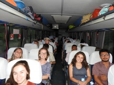 A group of smiling students sitting together inside a bus during their travels through the Serengeti.