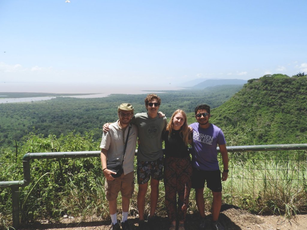 Four people pose together at a scenic overlook with a forested valley stretching out behind them.