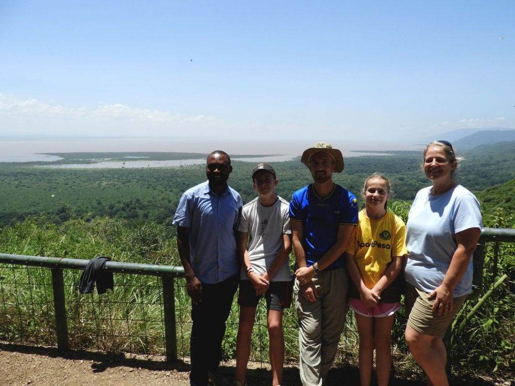 A group of five people, including children, poses at a scenic overlook with a river valley and green hills behind them.