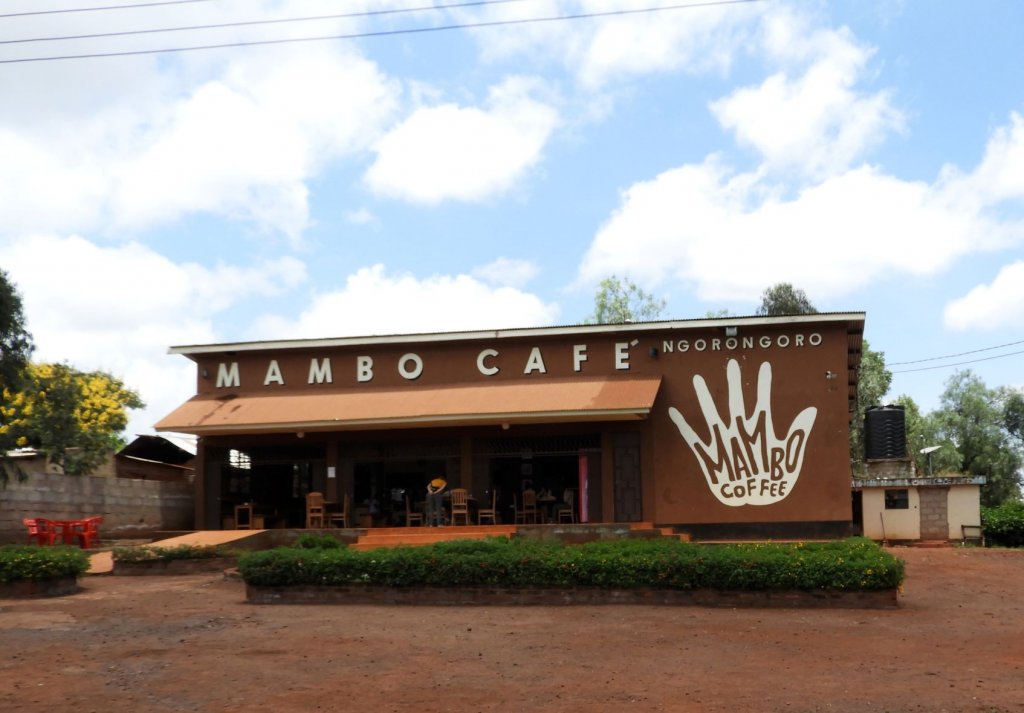 The exterior of the Mambo Cafe in Ngorongoro, a wooden building with a large stylized hand logo on its front.