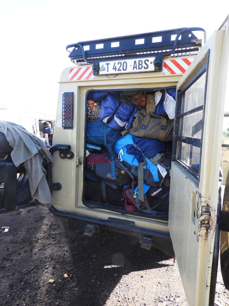 The open rear of a safari vehicle packed with duffel bags and blue luggage.