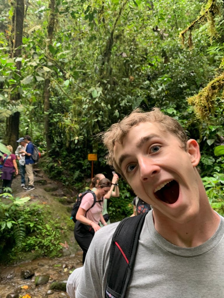 A young man with an excited, open-mouthed expression on a forest trail.