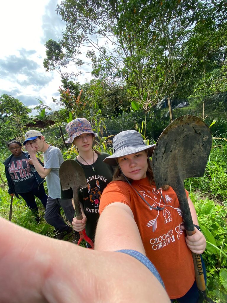 A group taking a selfie together outdoors with greenery in the background.