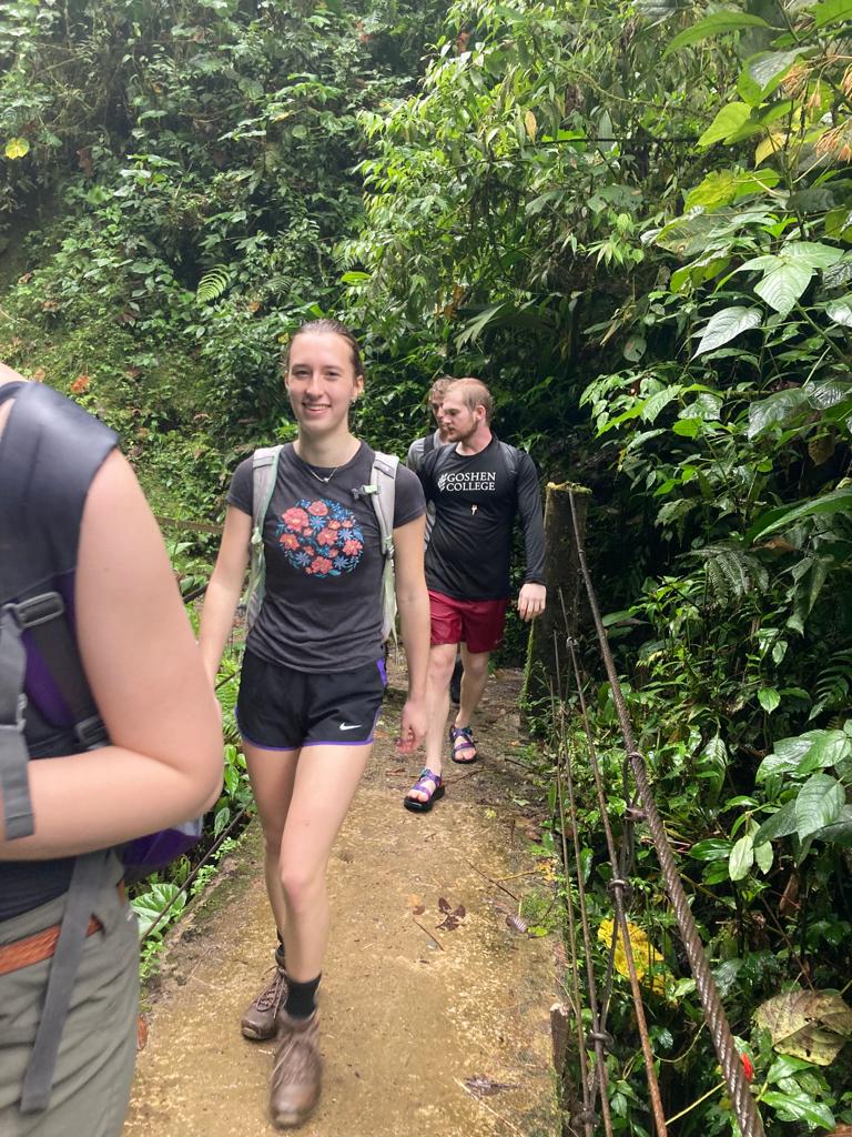 Two hikers walking together on a dirt trail through lush green forest.