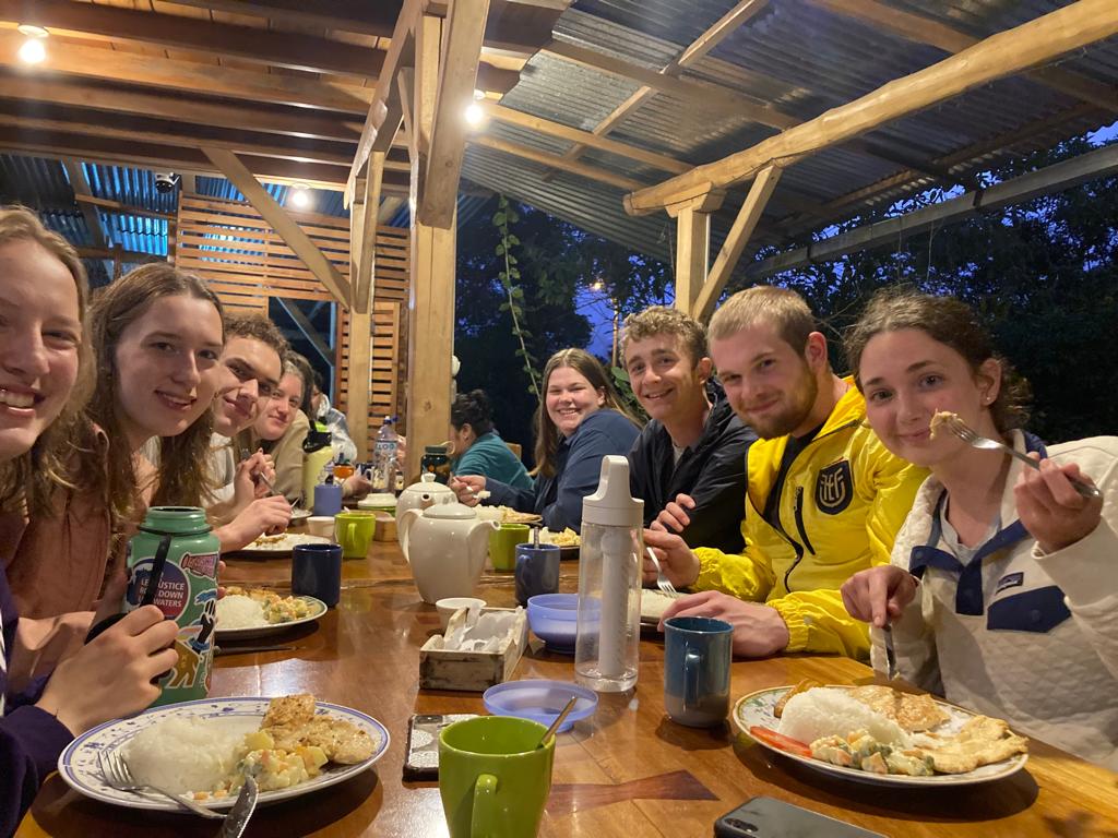 A group of people sharing a meal together at a long table under a covered patio.