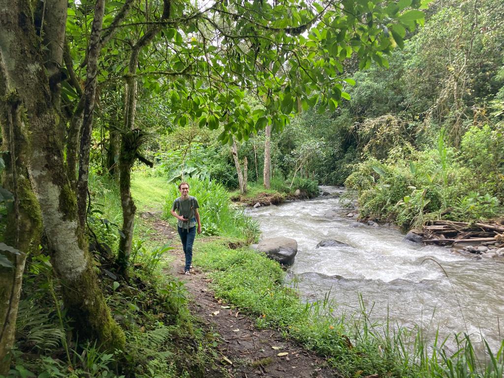 A group of students walking along a forest trail beside a river.