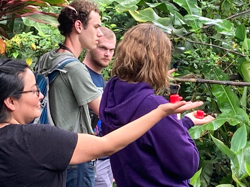 Two students holding a feeder as a hummingbird approaches.
