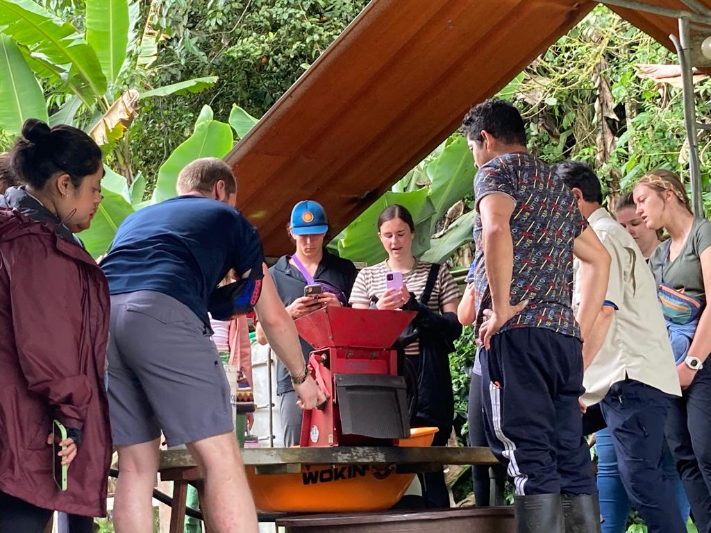 Students gathered around processing equipment at a coffee farm.