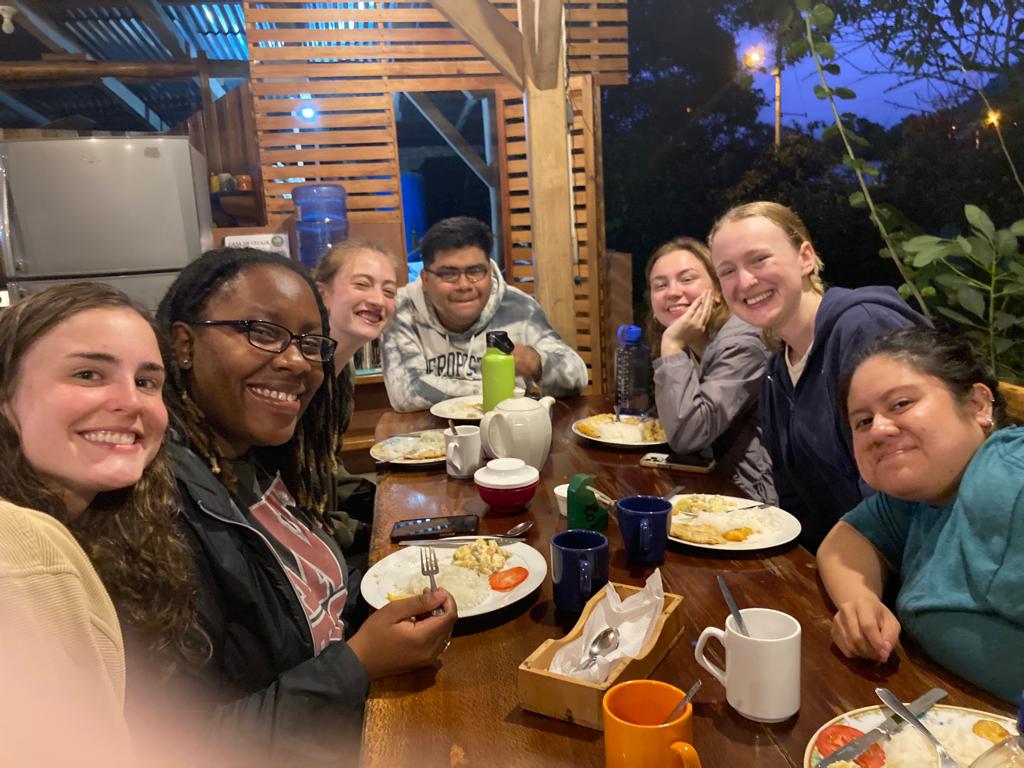 A cheerful group sharing food and drinks around a wooden table.