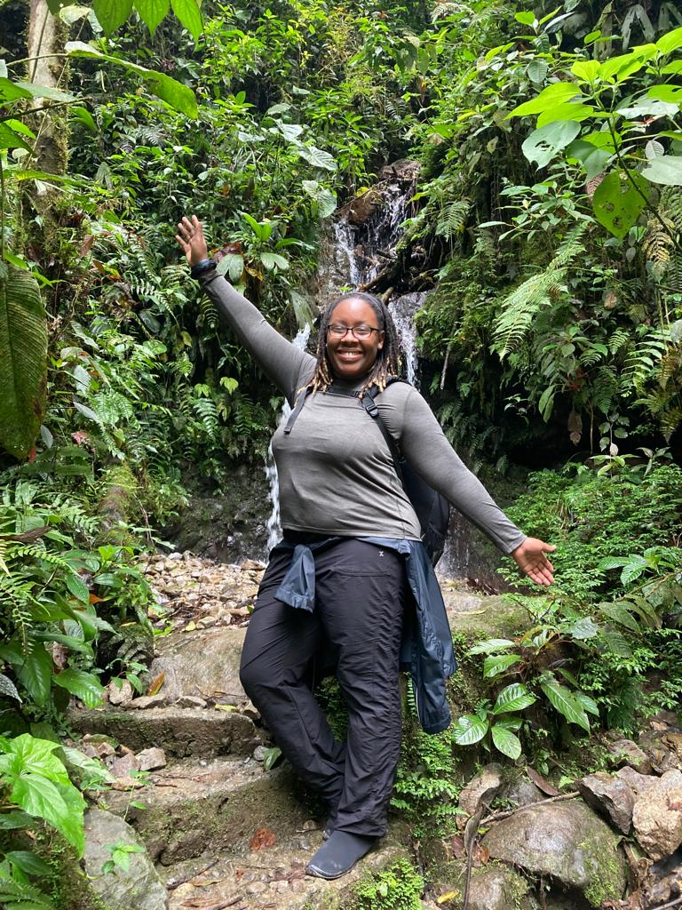 A person smiling and raising their arms joyfully on a forest trail.