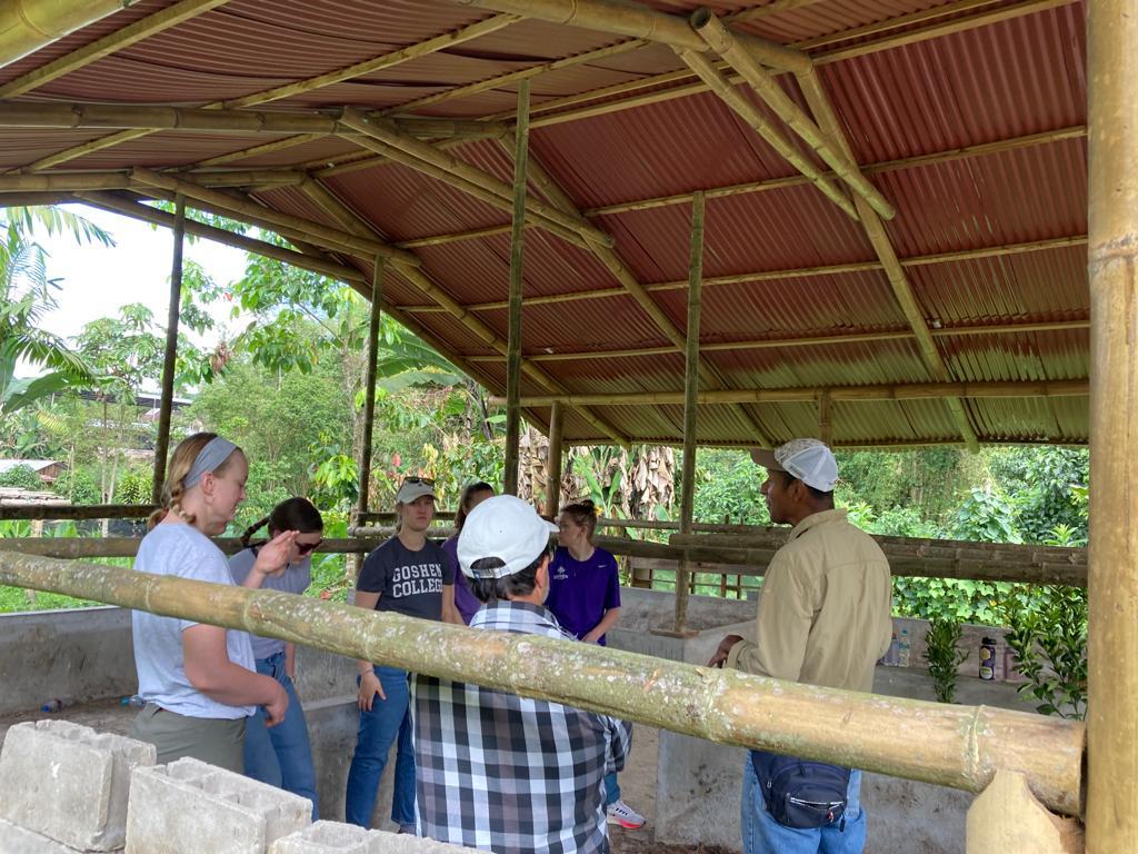 People gathered around a work table under a covered outdoor structure.
