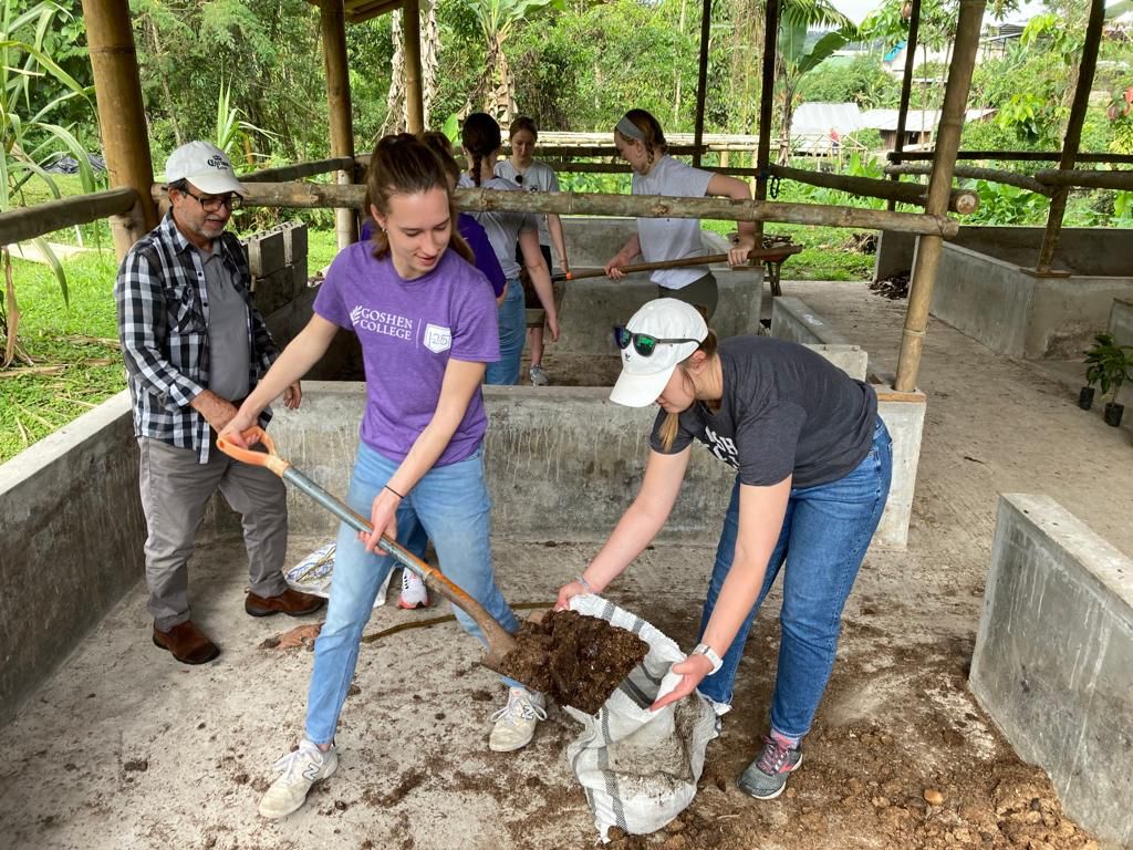 Students filling bags with soil using shovels at a farm.
