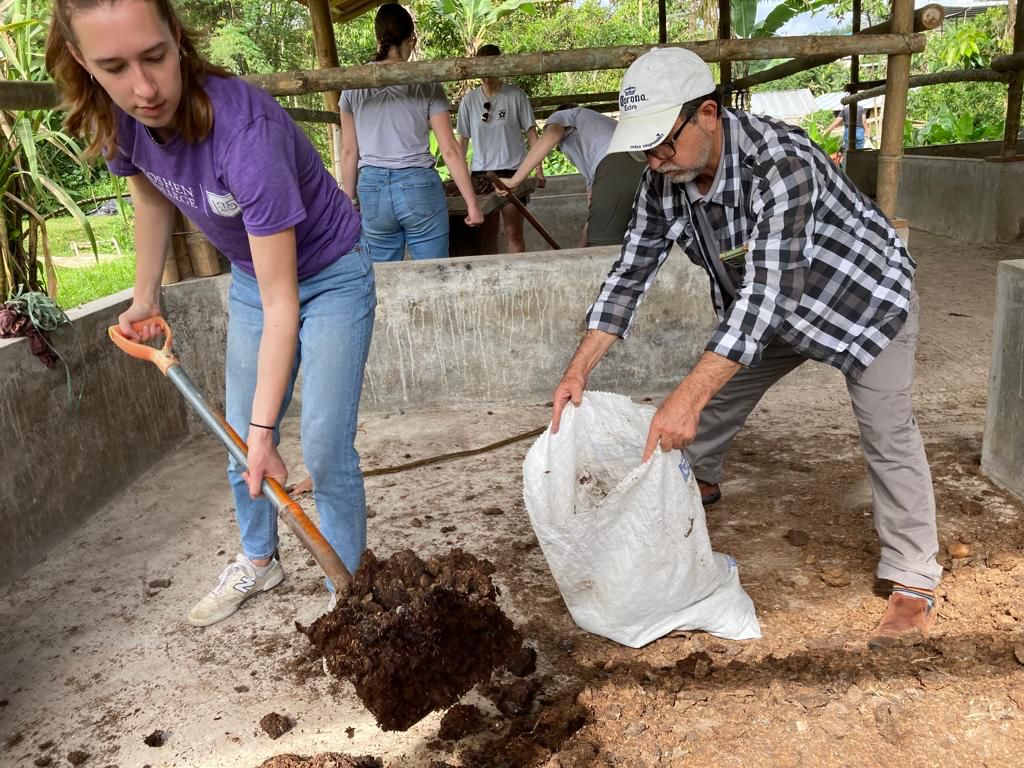 Two students shoveling soil into a bag on the ground.