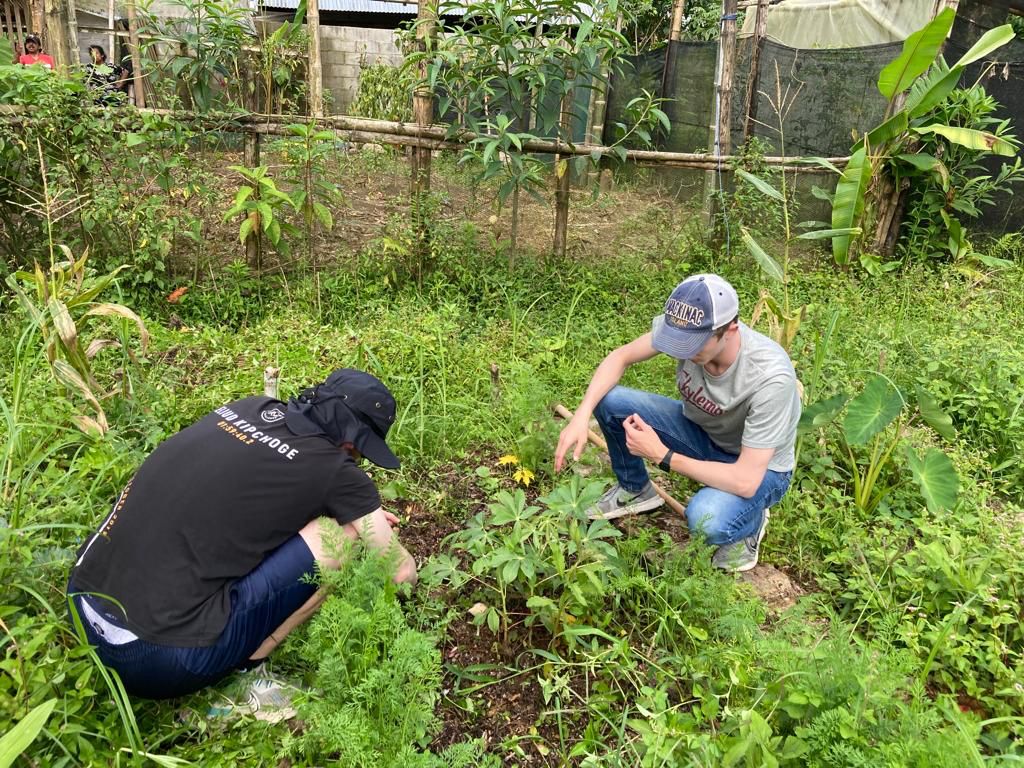 Two people kneeling to work with plants in a lush garden.
