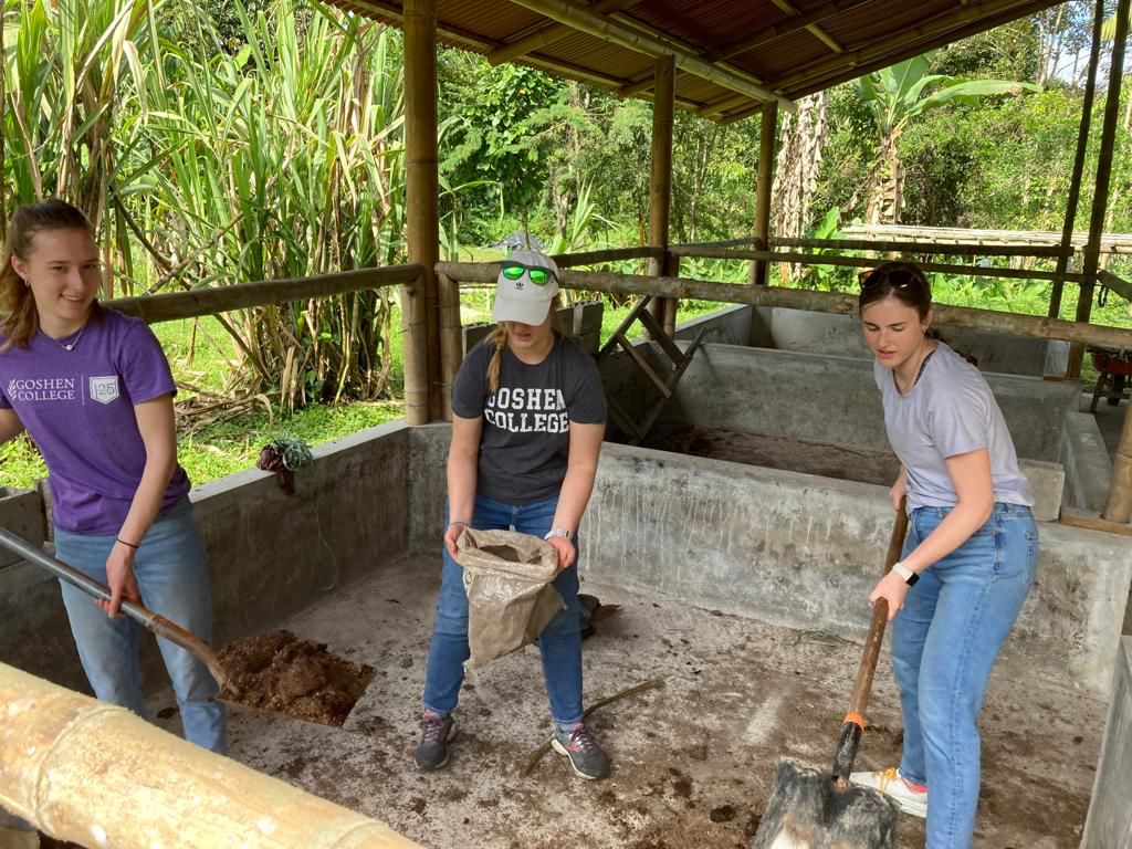 People working with soil at a raised bed under a covered shelter.