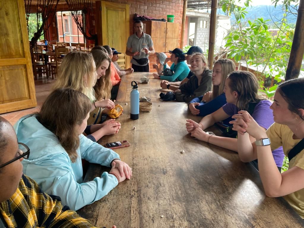 Students gathered around a long wooden table inside a building.