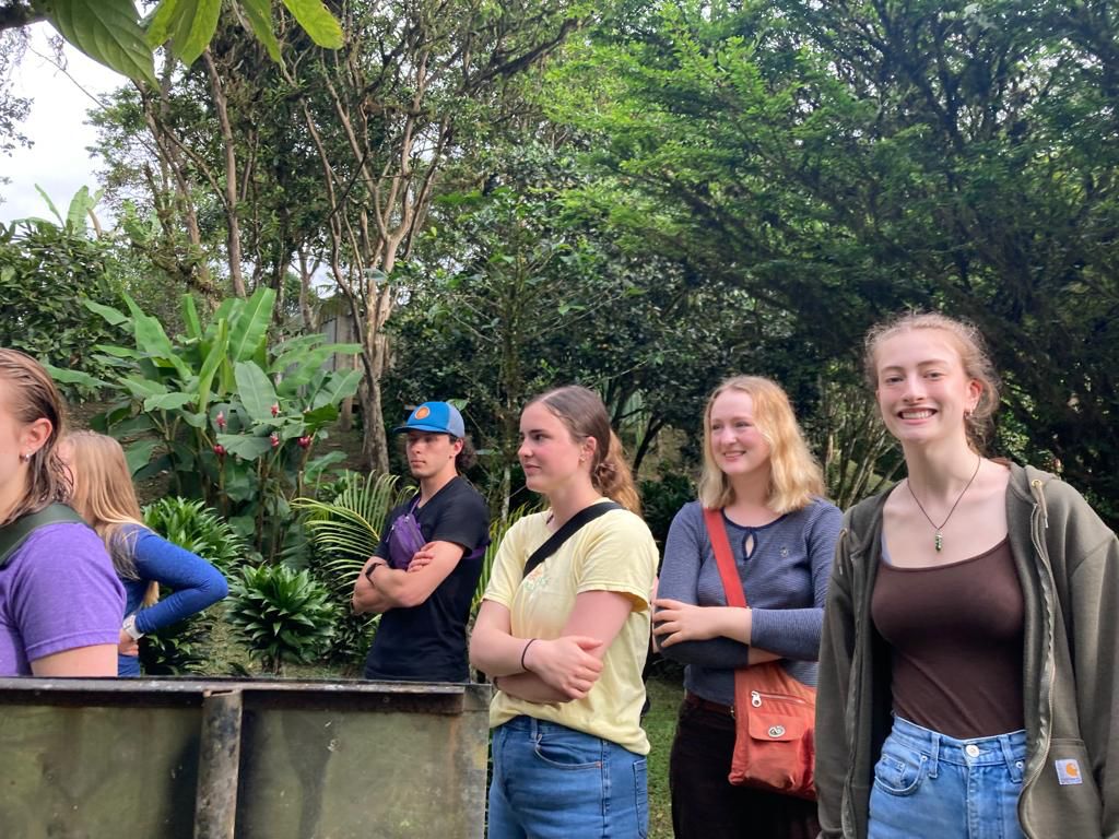 Young women standing together outdoors among plants and trees.