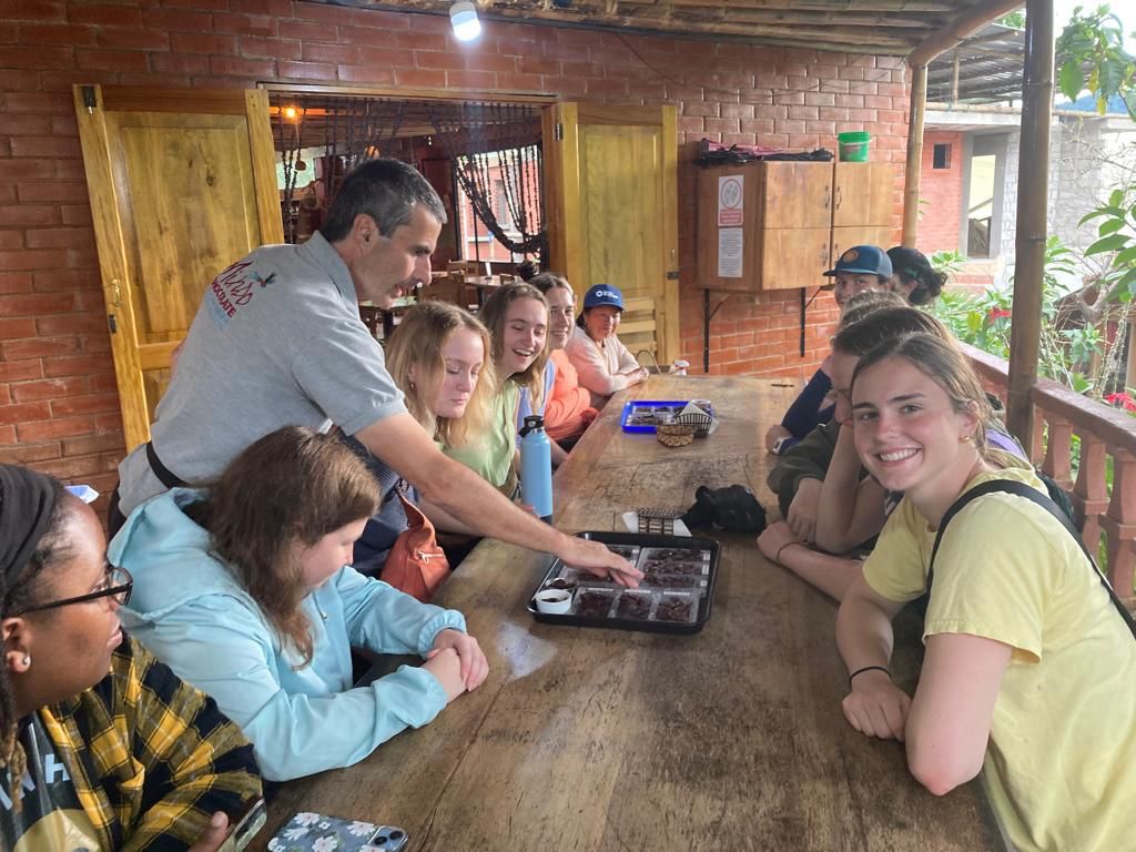 A person drinking from a mug at a wooden table with others.