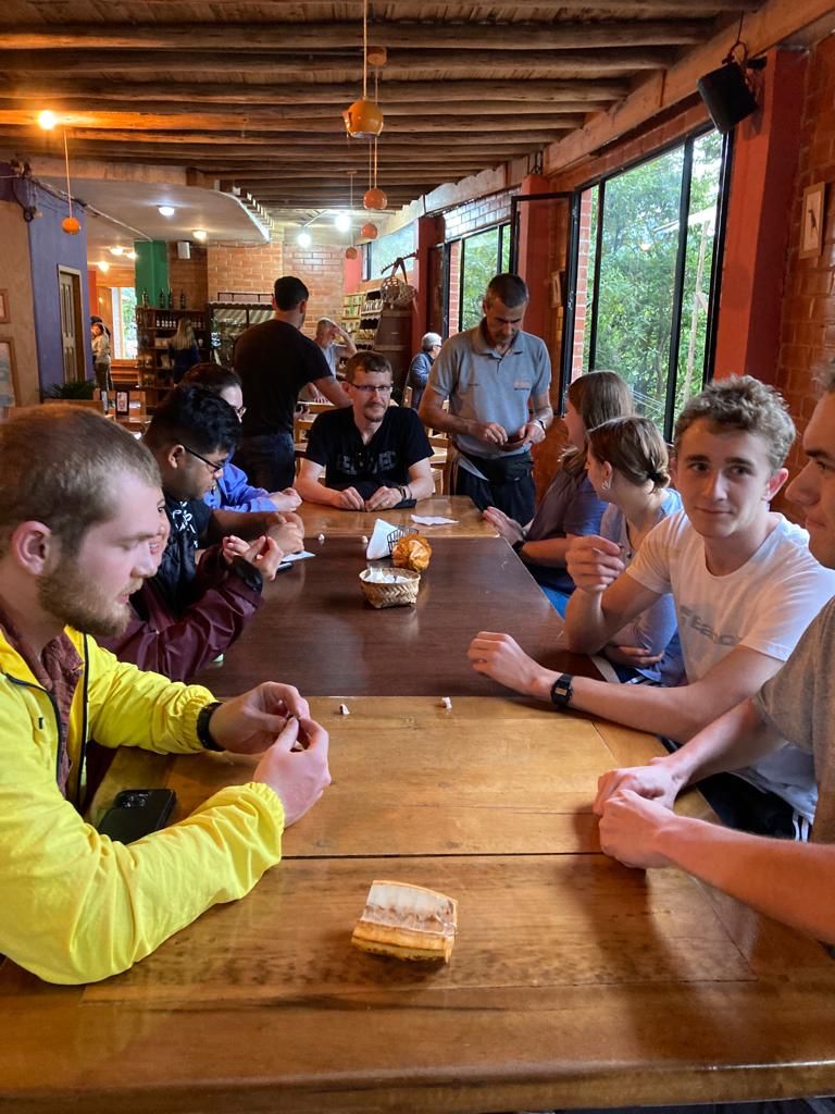 A smiling person taking a selfie with friends at a table in the evening.