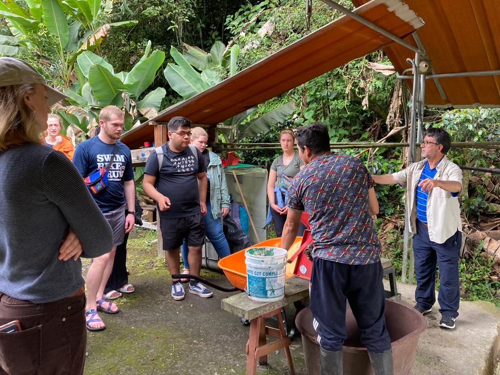 Students processing coffee with a hand-crank machine and large bowl.