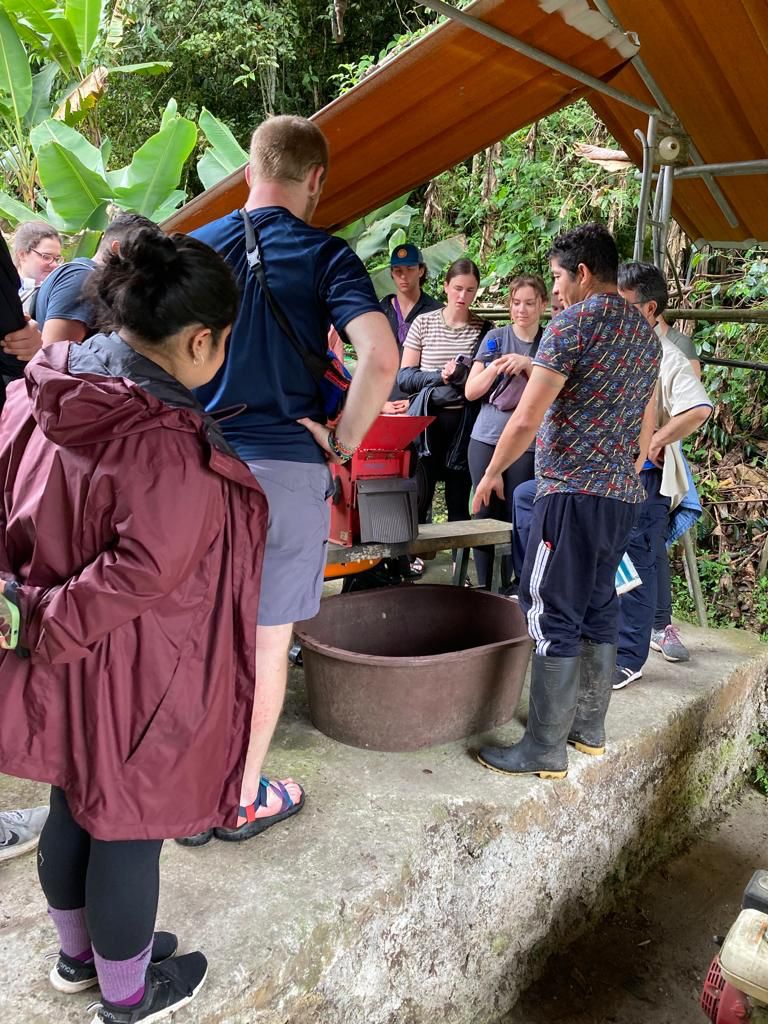 People working with a coffee grinder and pots under a covered area.