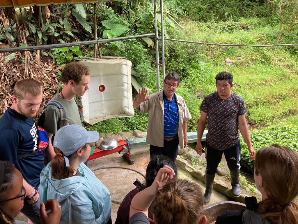 A group of students standing in a circle inside a greenhouse.