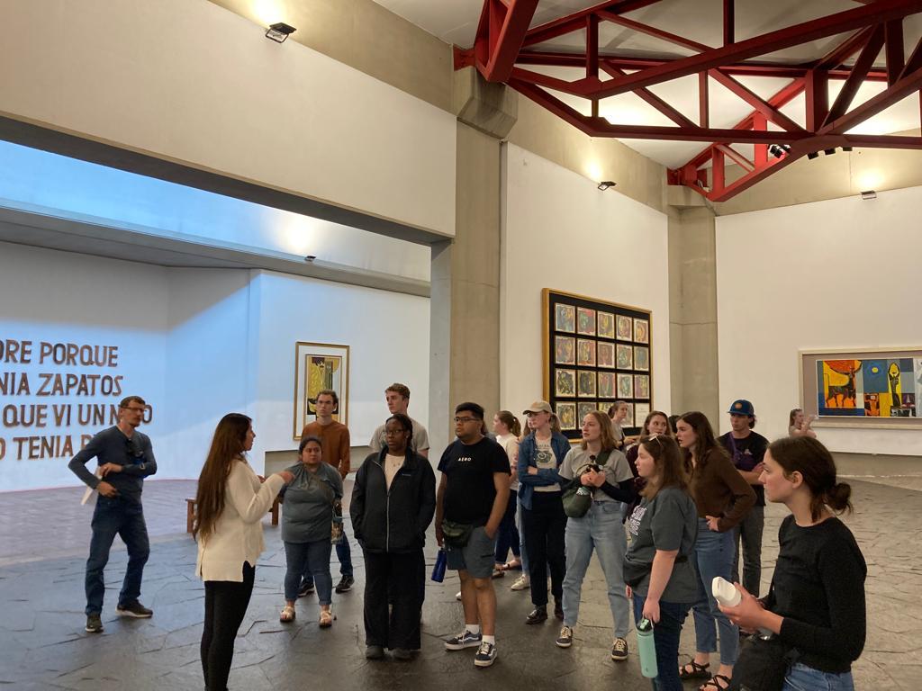 Students walking through a gallery with polished wood floors and paintings.