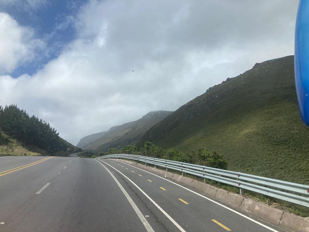 A curved mountain road with hills in the background, and a partly cloudy sky.