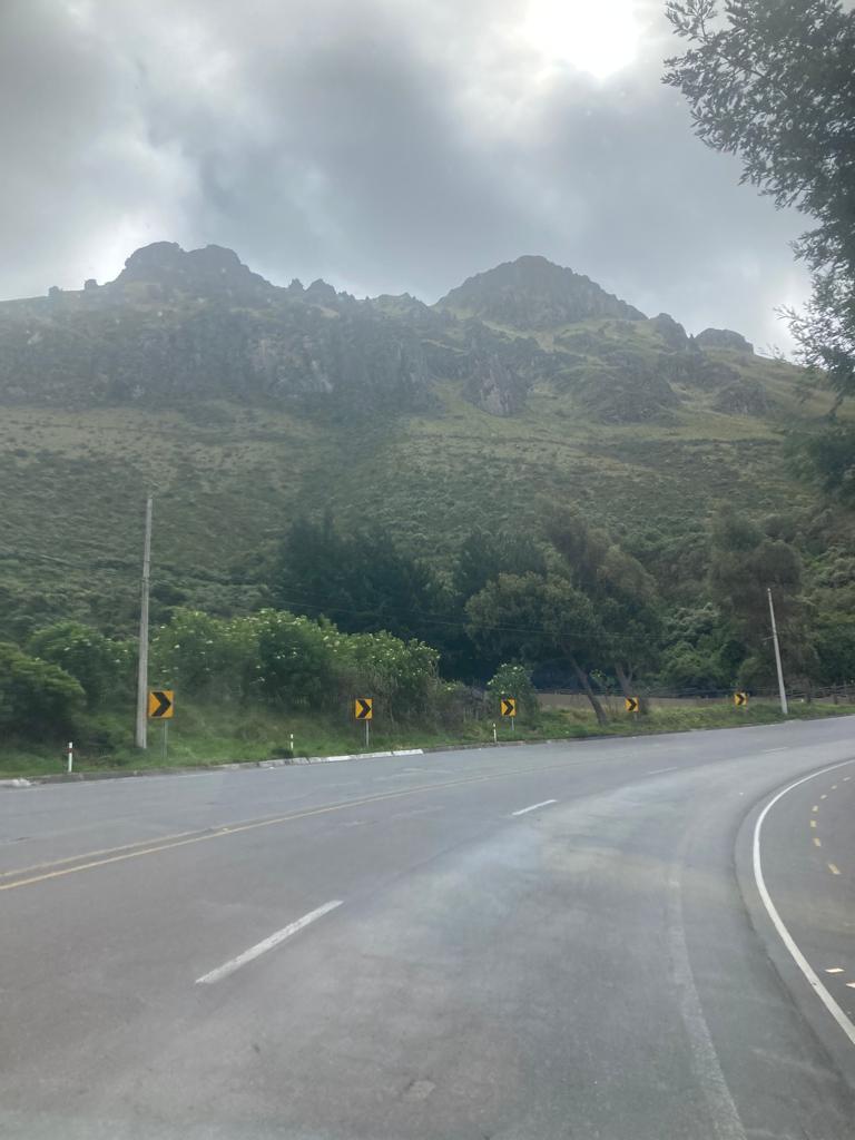 A winding highway in the mountains with green hills and rocky peaks under a cloudy sky.